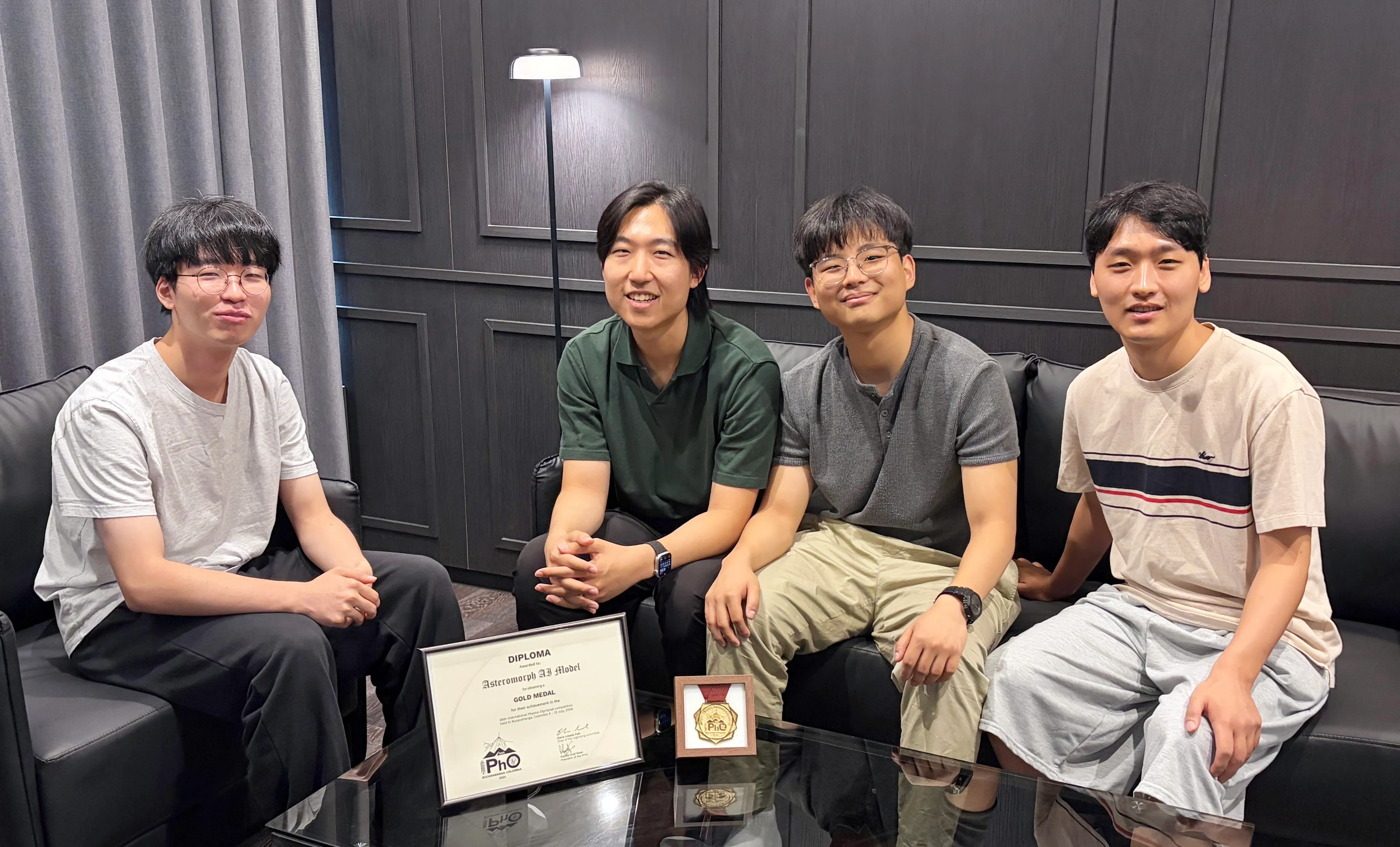 Our team members seated behind a table holding the framed IPhO diploma awarded to the "Asteromorph AI Model" for a gold medal, next to the medal in its case.